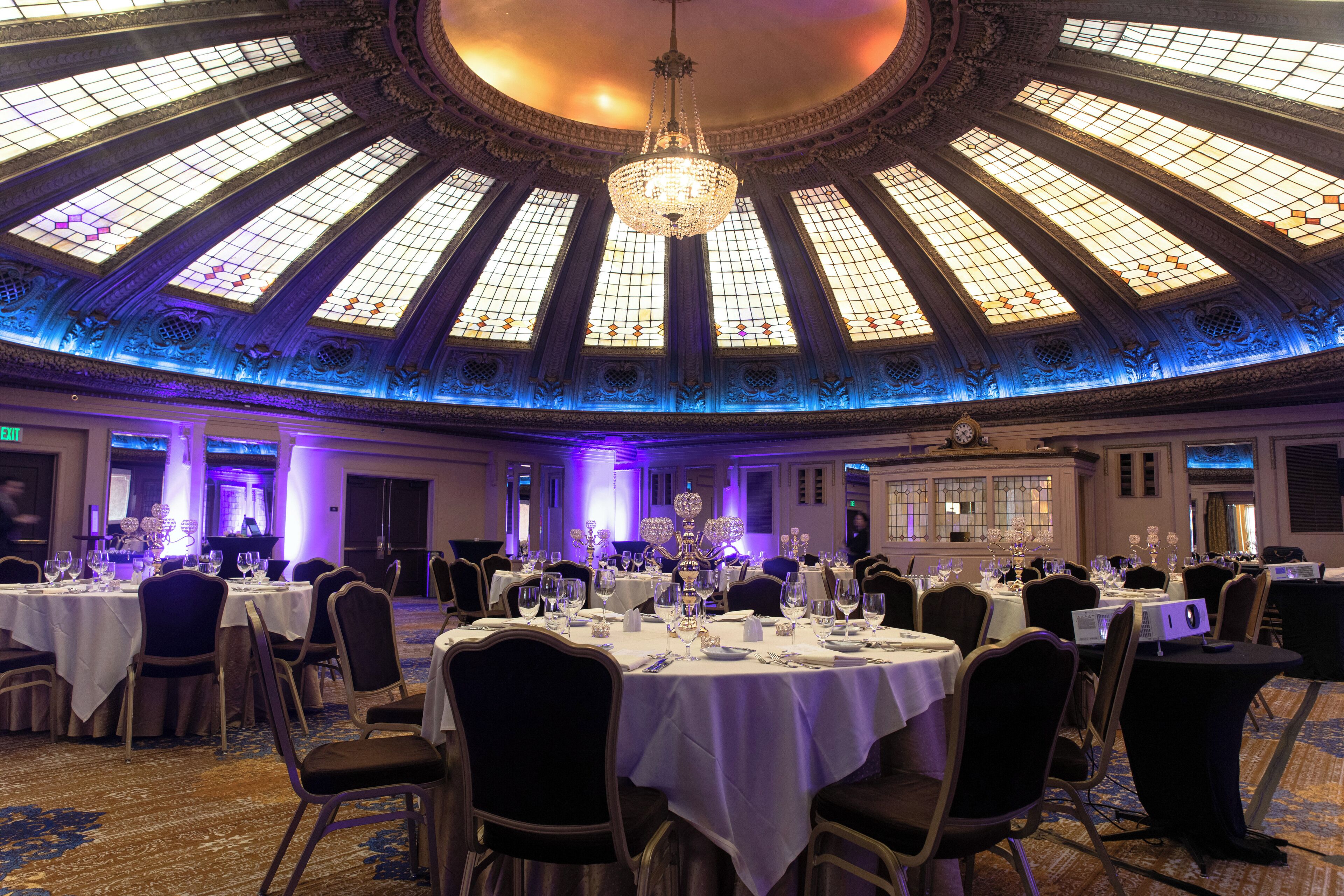 A banquet hall with round tables, chairs, and a large chandelier.