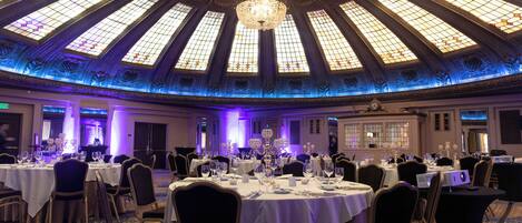 A banquet hall with round tables, chairs, and a large chandelier.