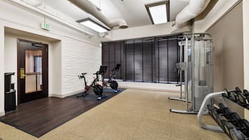 Uma academia com bicicletas ergométricas, um banco de musculação e halteres.