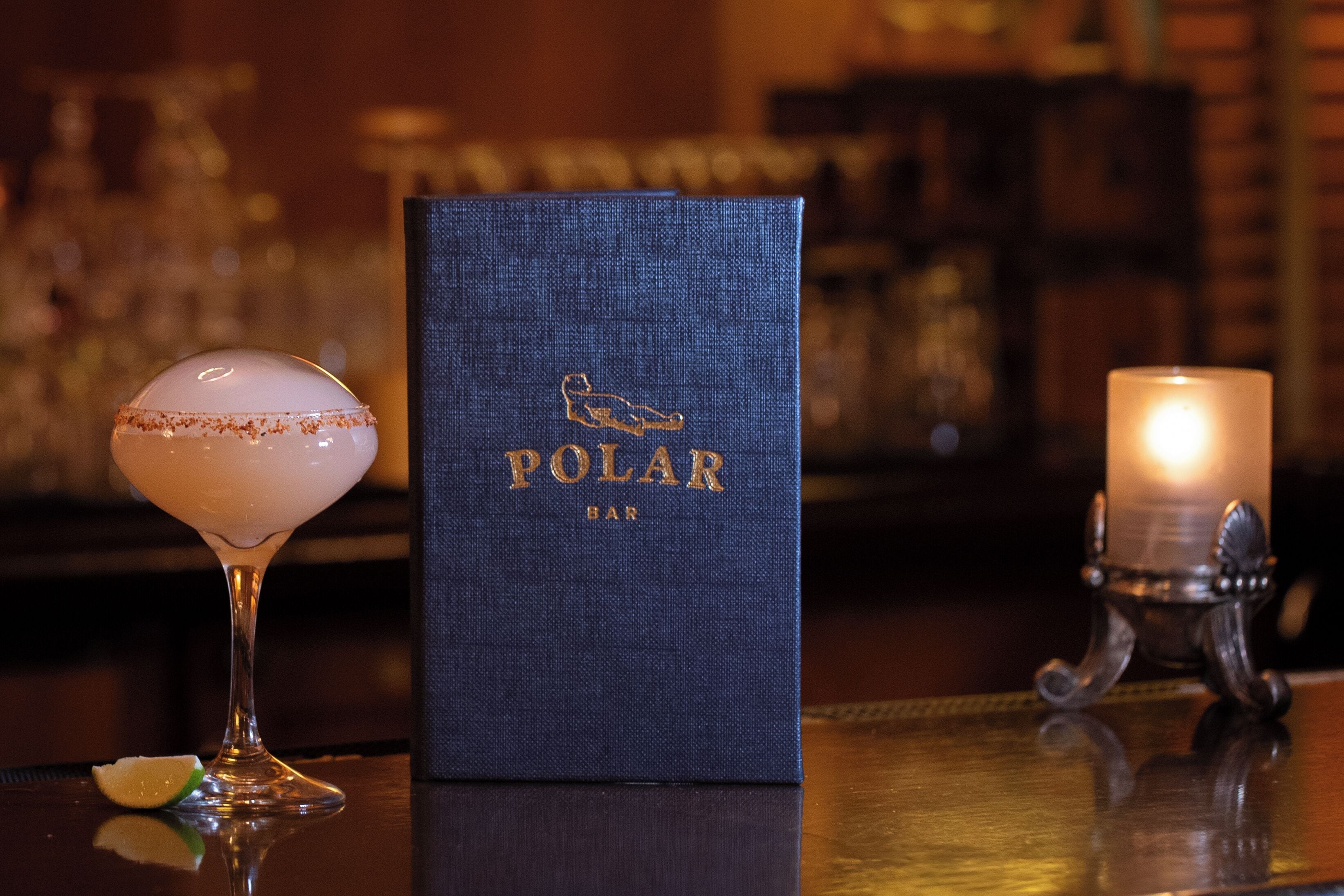 Un bar con una copa de cóctel, un libro azul y una vela.