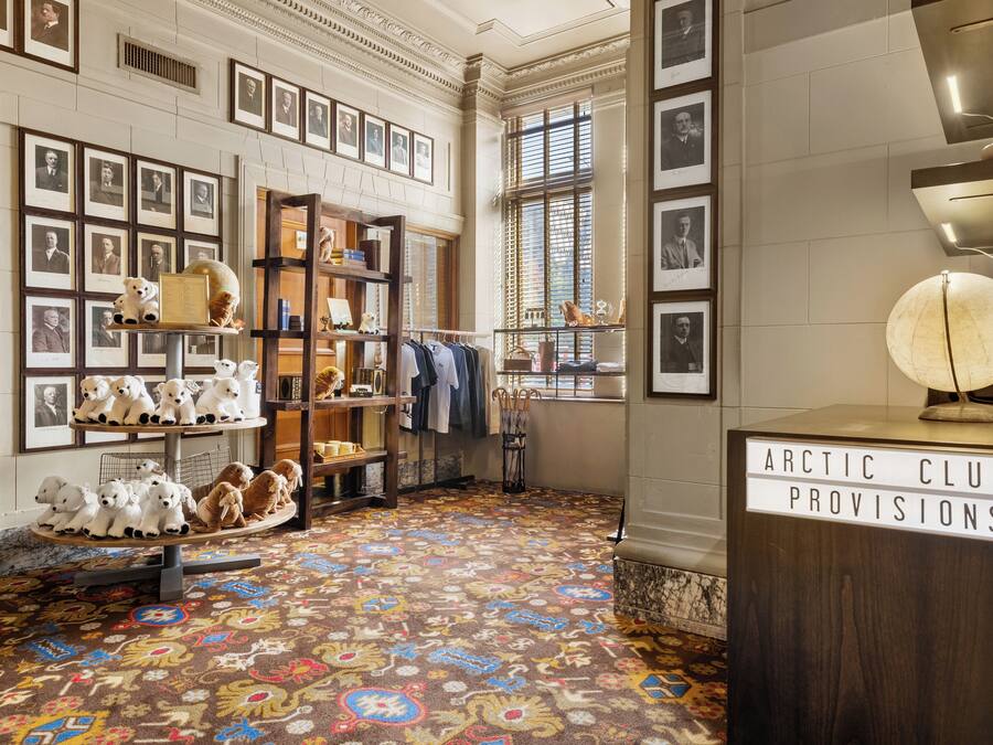 A room with a patterned carpet, shelves with framed photos, and a sign reading "ARCTIC CLUB PROVISIONS".