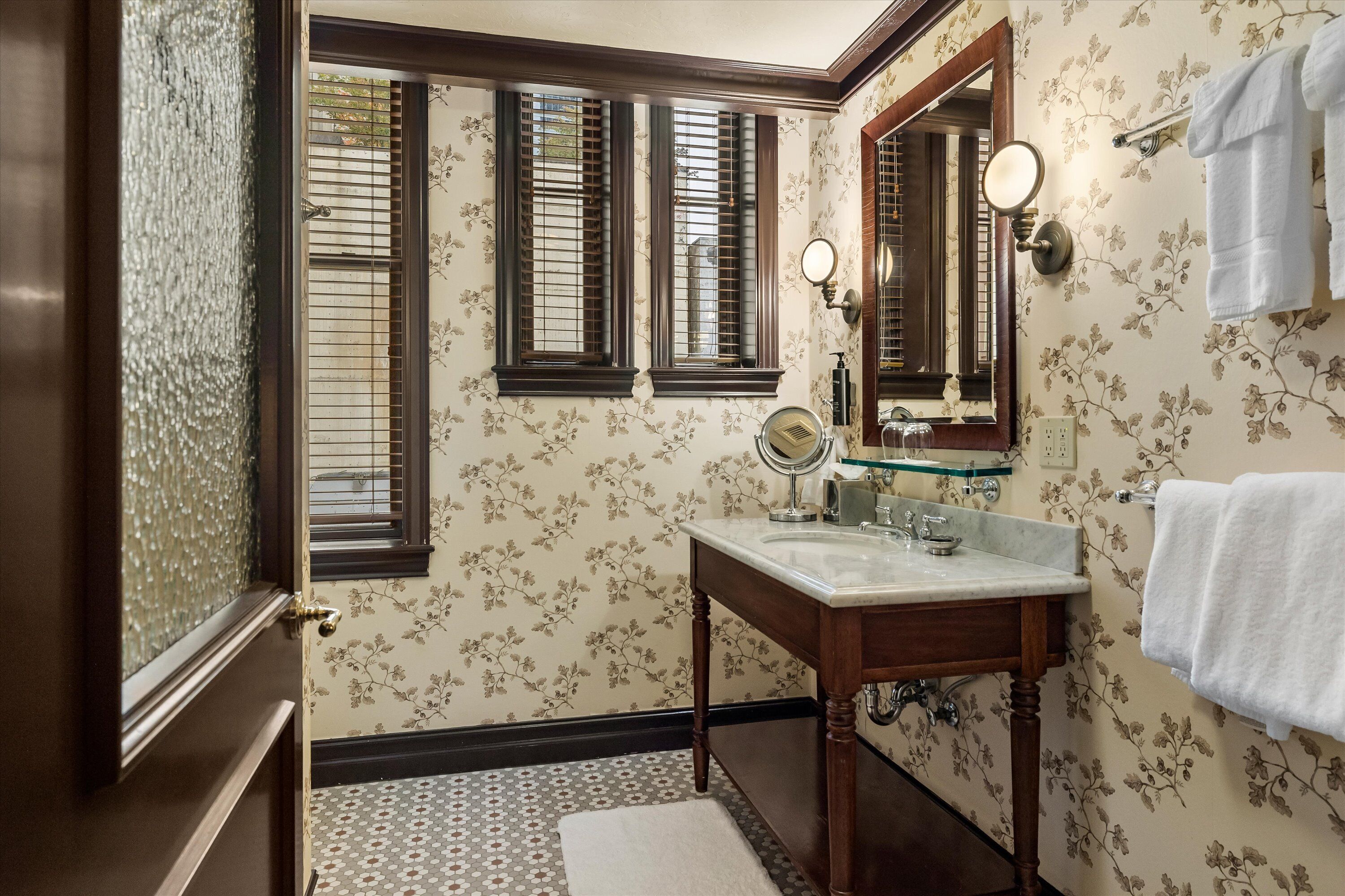 A bathroom with a wooden vanity, a mirror, and a window with blinds.