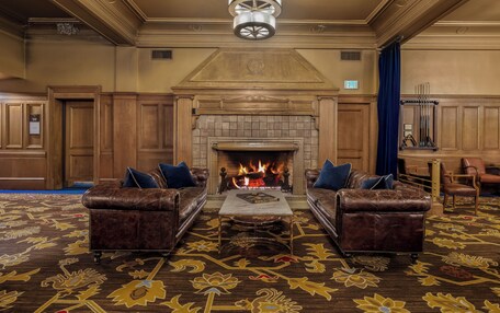 A spacious room with a large fireplace, two leather sofas with blue cushions, and a patterned carpet.