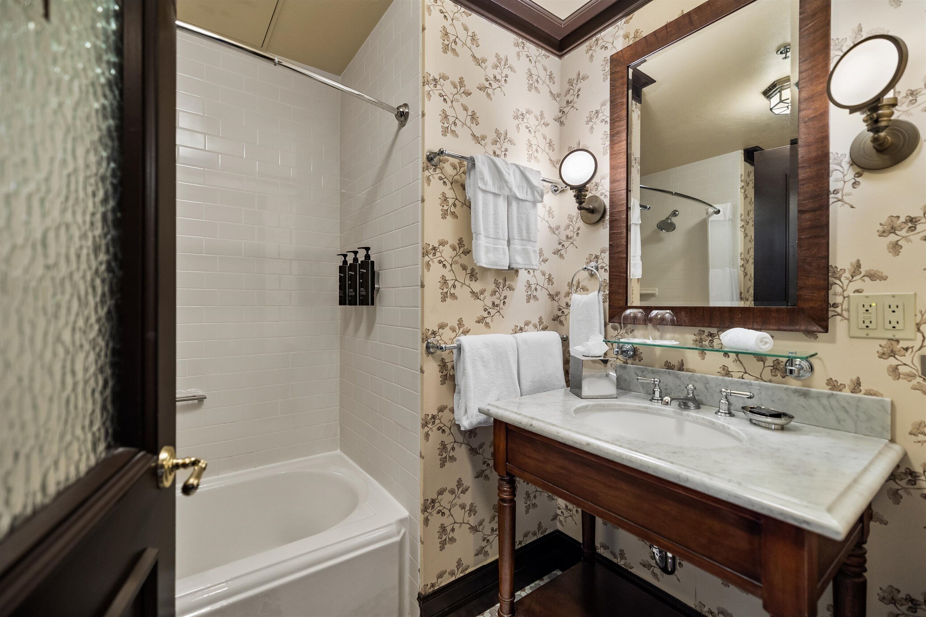 A bathroom with a bathtub, a sink, a mirror, and floral wallpaper.