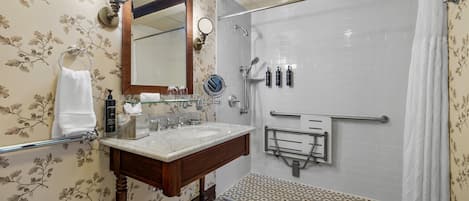 Un baño con tocador de madera, un espejo grande, ducha con puerta de vidrio y piso estampado.