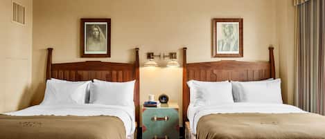 A hotel room with two beds, a nightstand with a lamp, and framed artwork on the walls.