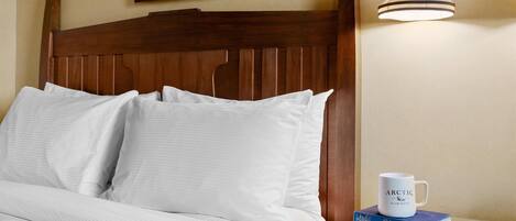 A neatly made bed with white linens, a wooden headboard, and a bedside table with a white mug and books.