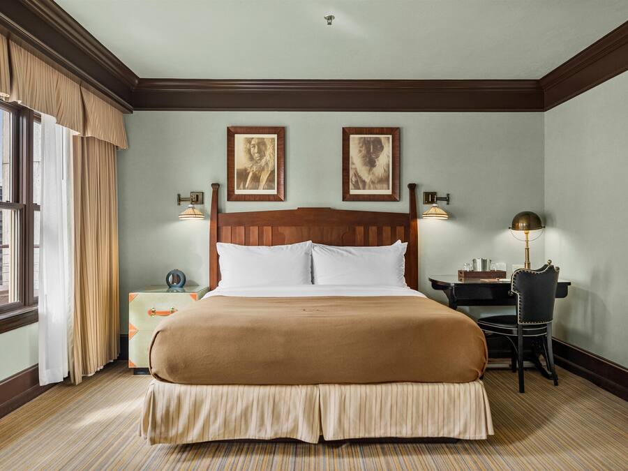 A hotel room with a large bed, a desk, a chair, and two framed pictures on the wall.