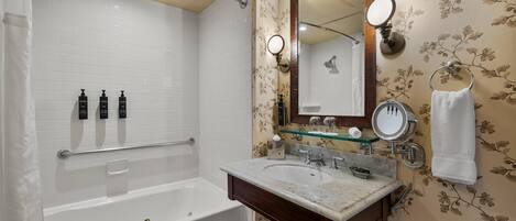A bathroom with a bathtub, two sinks, a mirror, and toiletries.