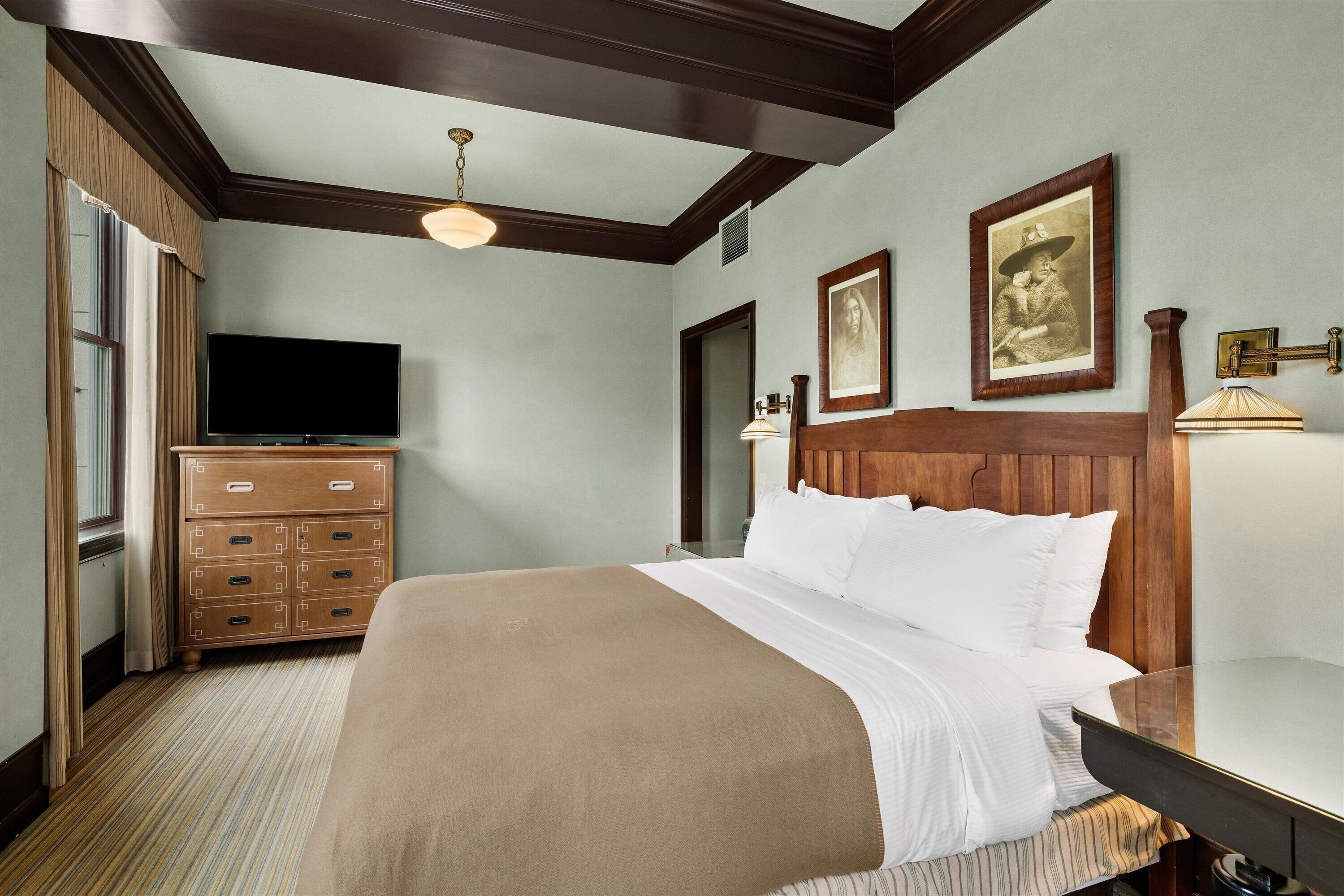 Ein Hotelzimmer mit einem großen Bett, einem Holzkopfstück, einem Fernseher und einem Schminktisch.