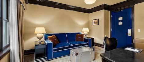 A hotel room with a blue sofa, two lamps, a small table, a suitcase, and a door.