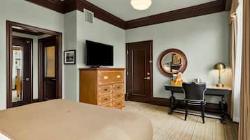Quarto de hotel com uma cama grande, uma cômoda de madeira, uma escrivaninha com cadeira, uma televisão, um espelho e um abajur.