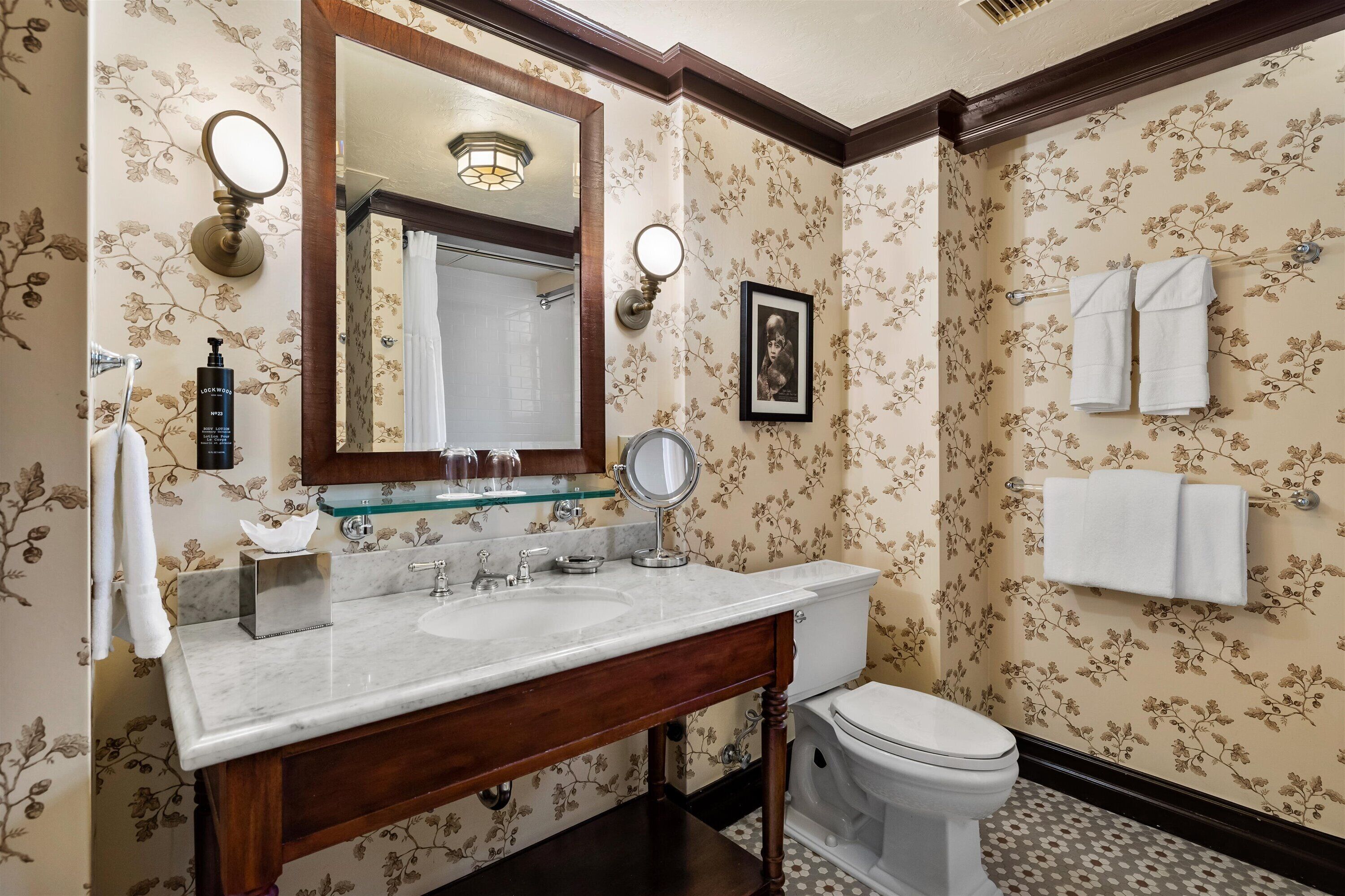 A bathroom with a marble sink, wooden vanity, a toilet, and floral wallpaper.