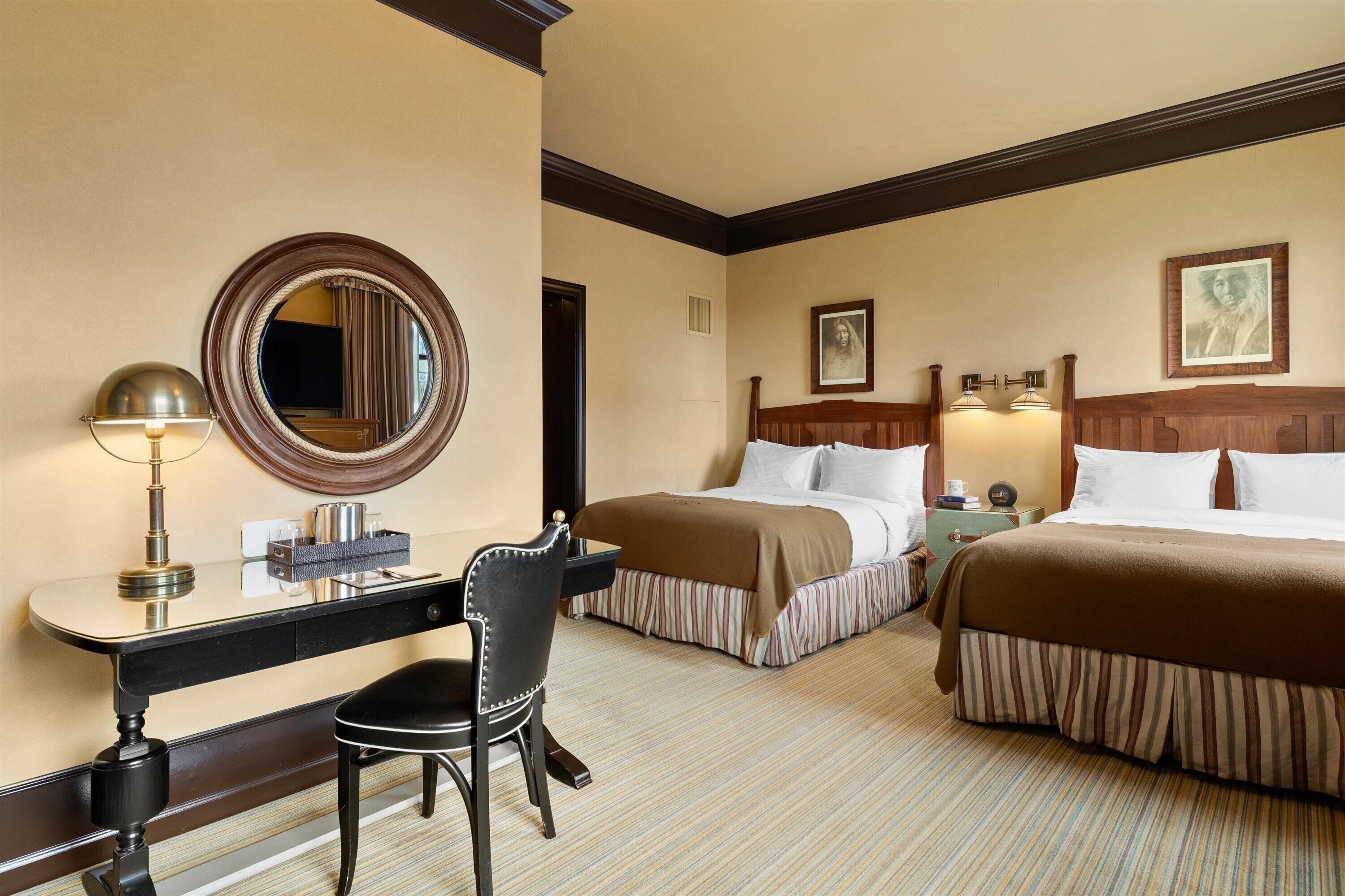 Ein Hotelzimmer mit zwei Betten, einem Schreibtisch mit Lampe, einem Sessel und einem großen Spiegel.