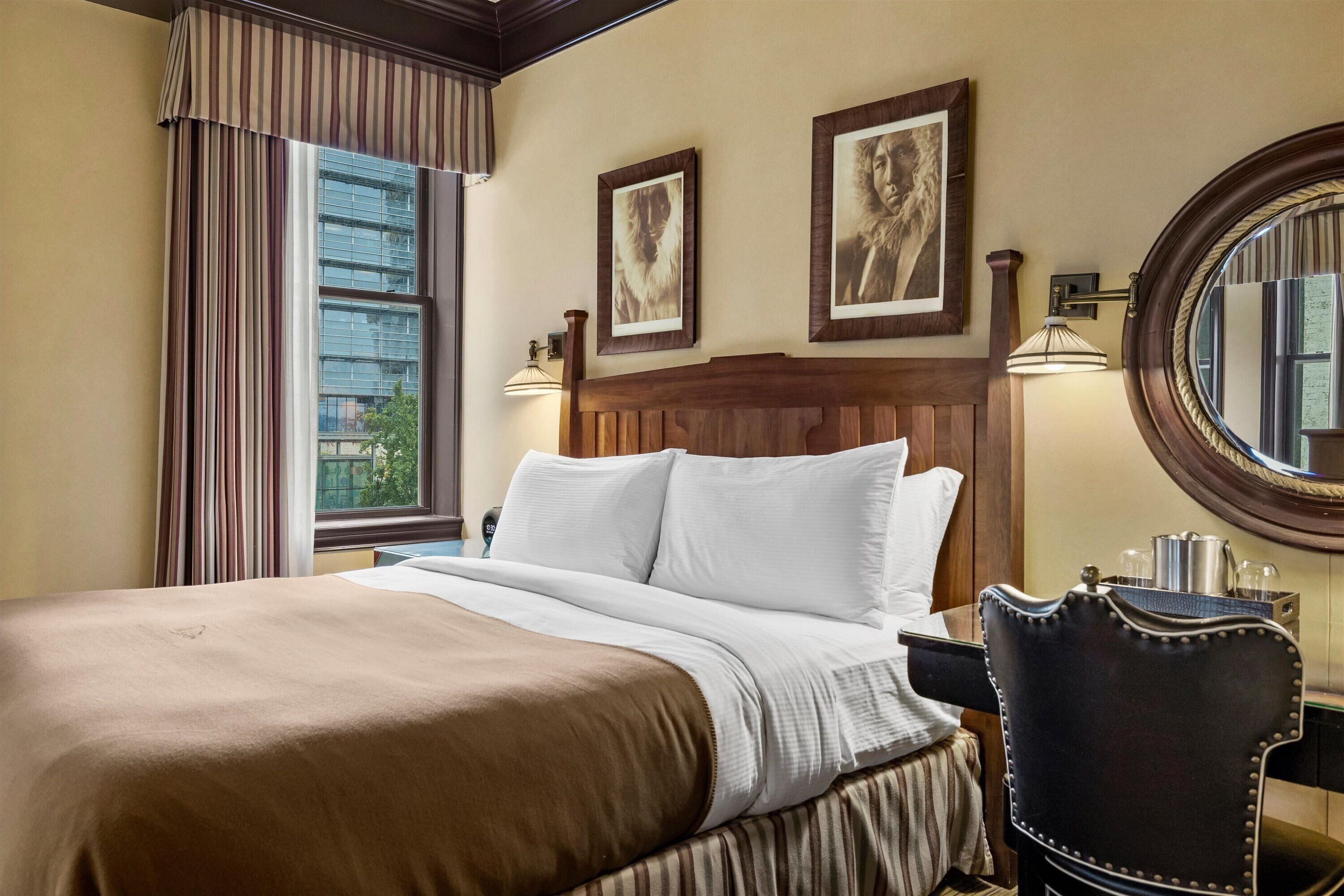 A hotel room with a large bed, a wooden headboard, a round mirror, and two framed pictures on the wall.