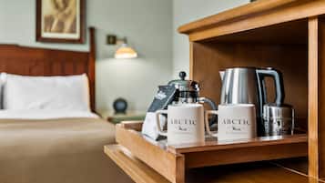 A wooden tray with two white mugs labeled "Arctic Club Hotel," a silver coffee pot, and a silver electric kettle on a hotel bed.