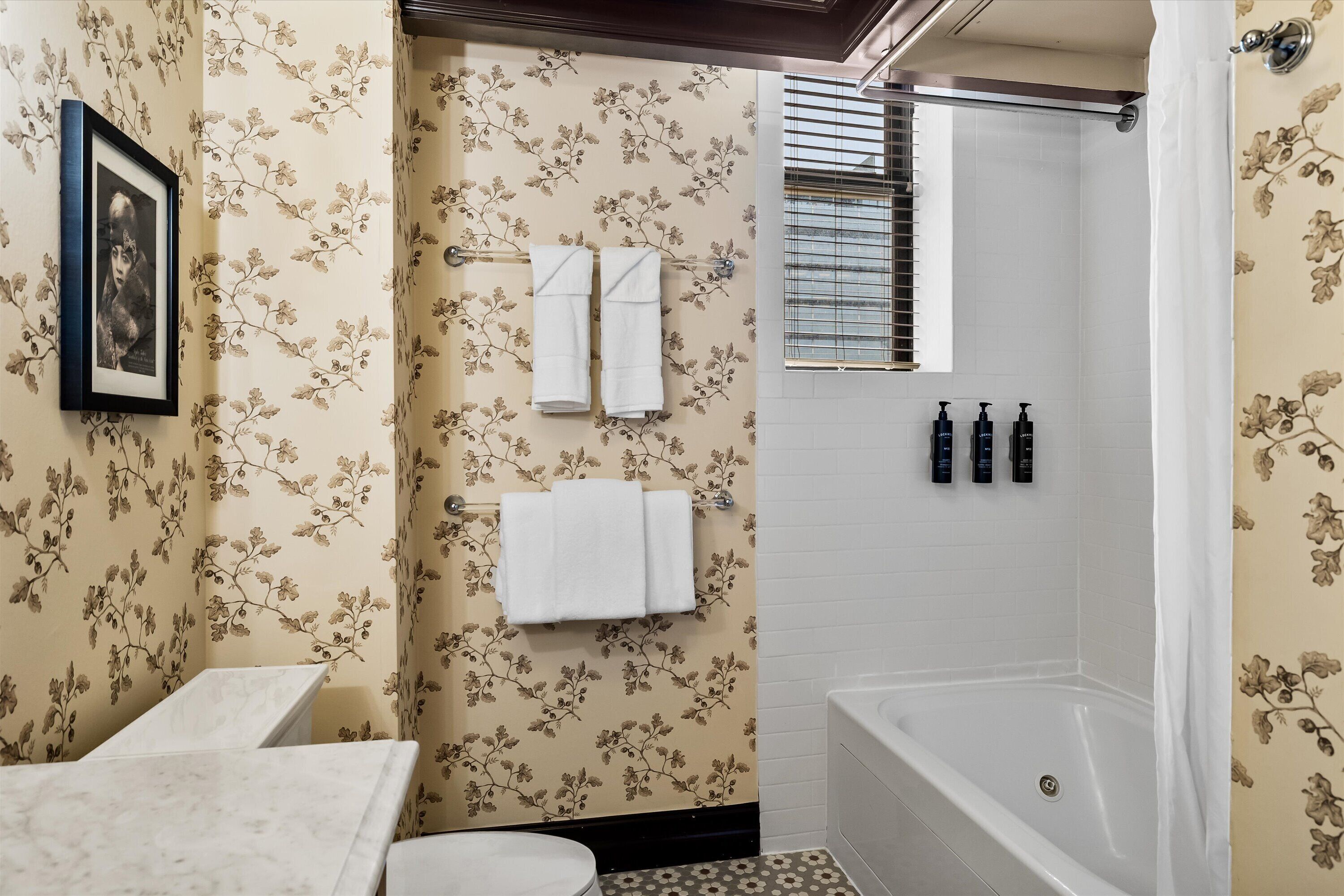 A bathroom with floral wallpaper, a bathtub, a toilet, and a framed picture on the wall.