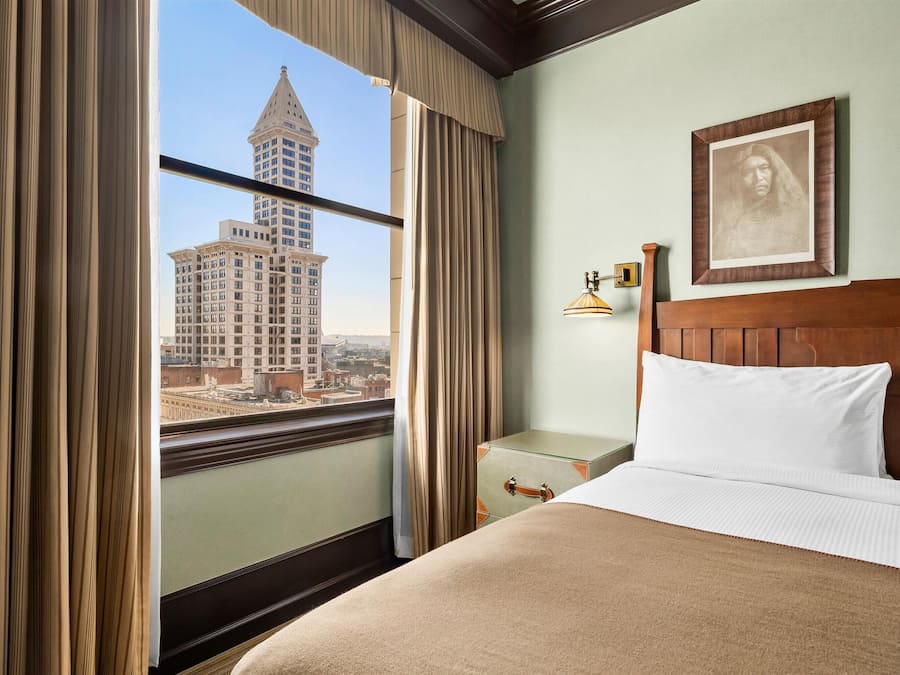 Habitación de hotel con un ventanal grande, una cama, una mesita de noche y un cuadro en la pared.