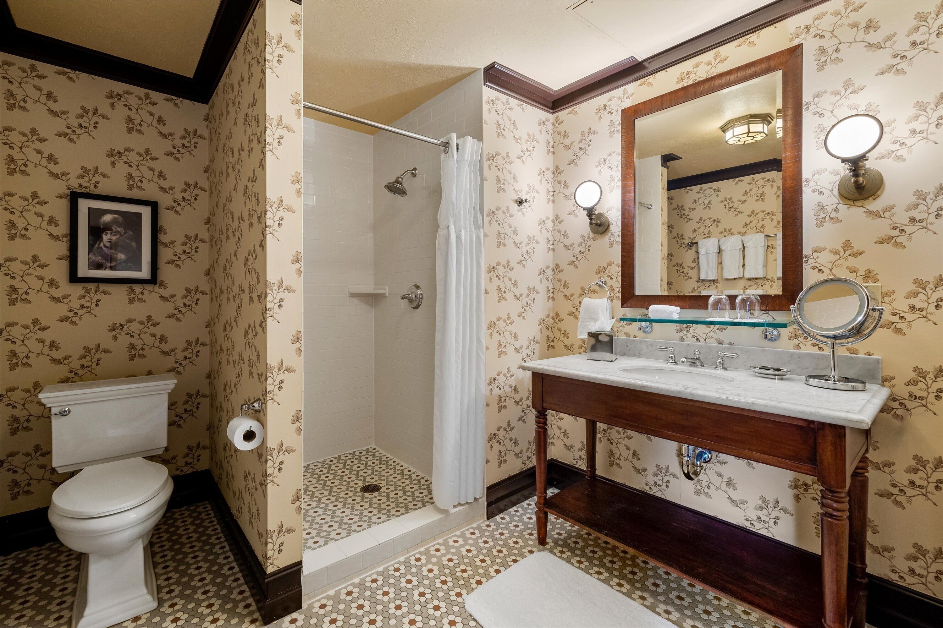A bathroom with a toilet, shower, and vanity with a mirror.