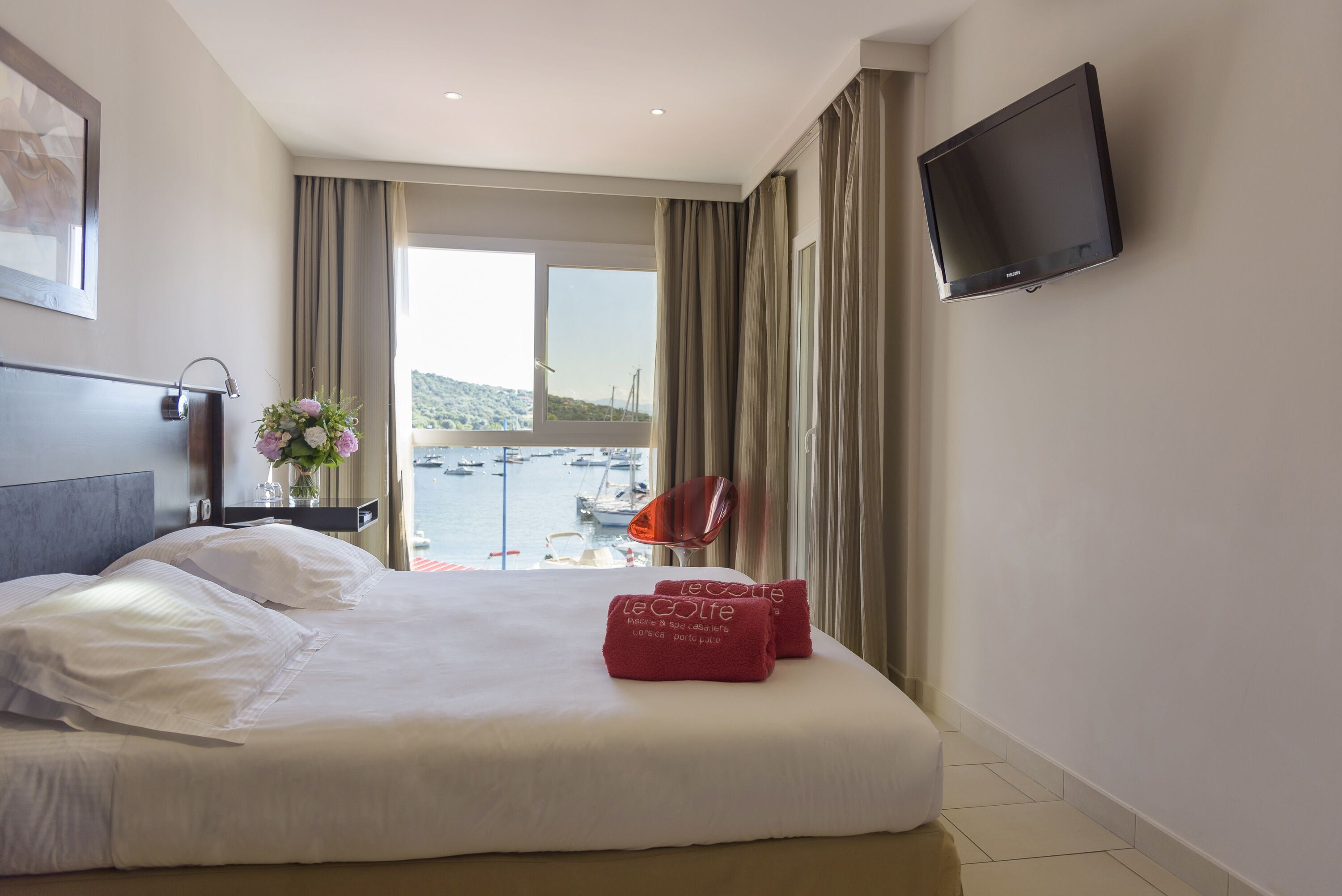 Ein Hotelzimmer mit einem großen Bett, einem Flachbildfernseher, Meerblick und einem Sessel am Fenster.