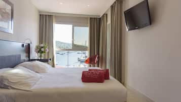 Habitación de hotel con una cama grande, un televisor de pantalla plana, vistas al mar y una silla junto a la ventana.