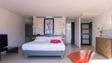 A modern hotel room with a large bed, a TV, a wooden dresser, and a bright red chair.