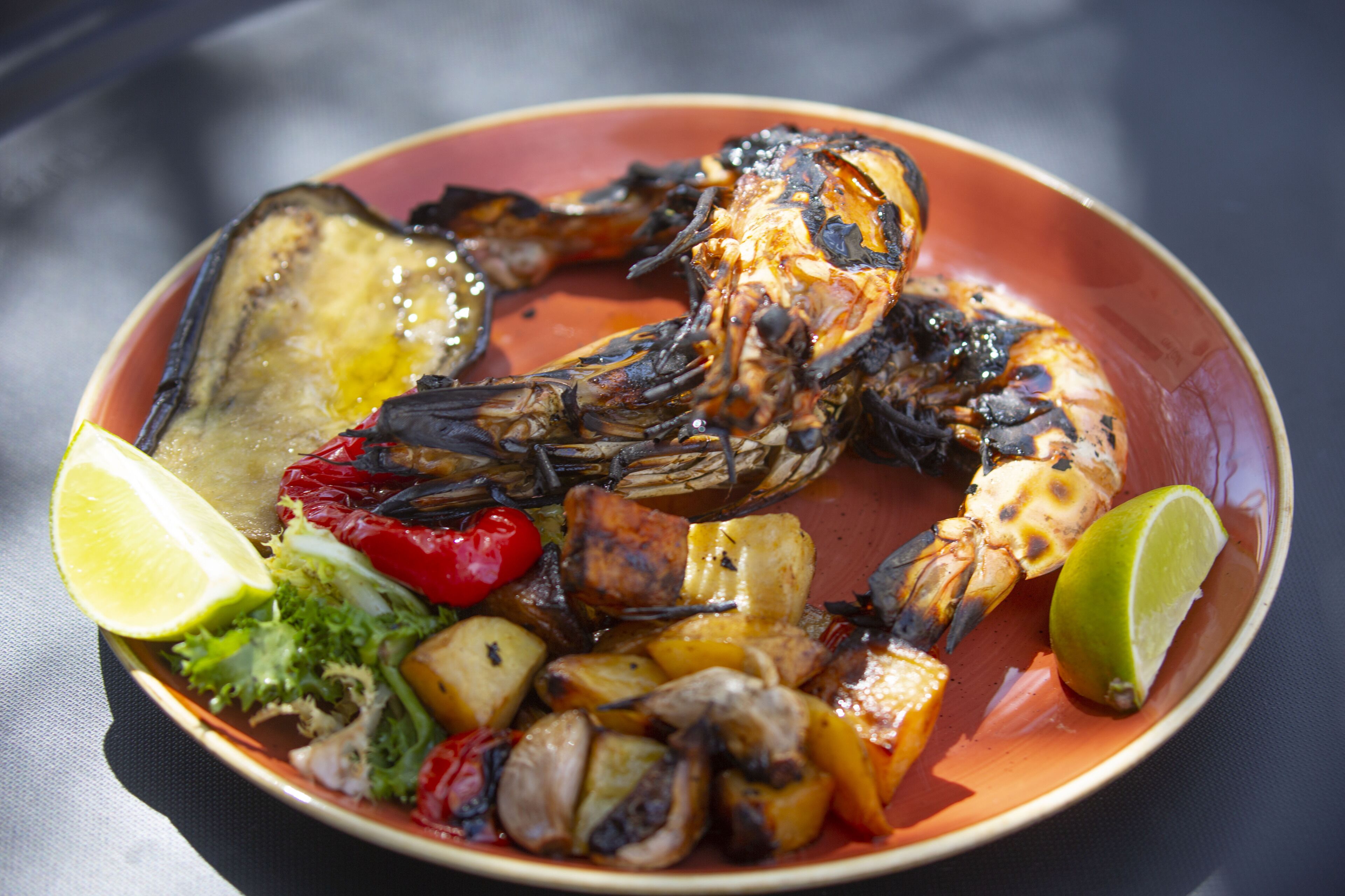 A plate of grilled seafood with vegetables and lime wedges.
