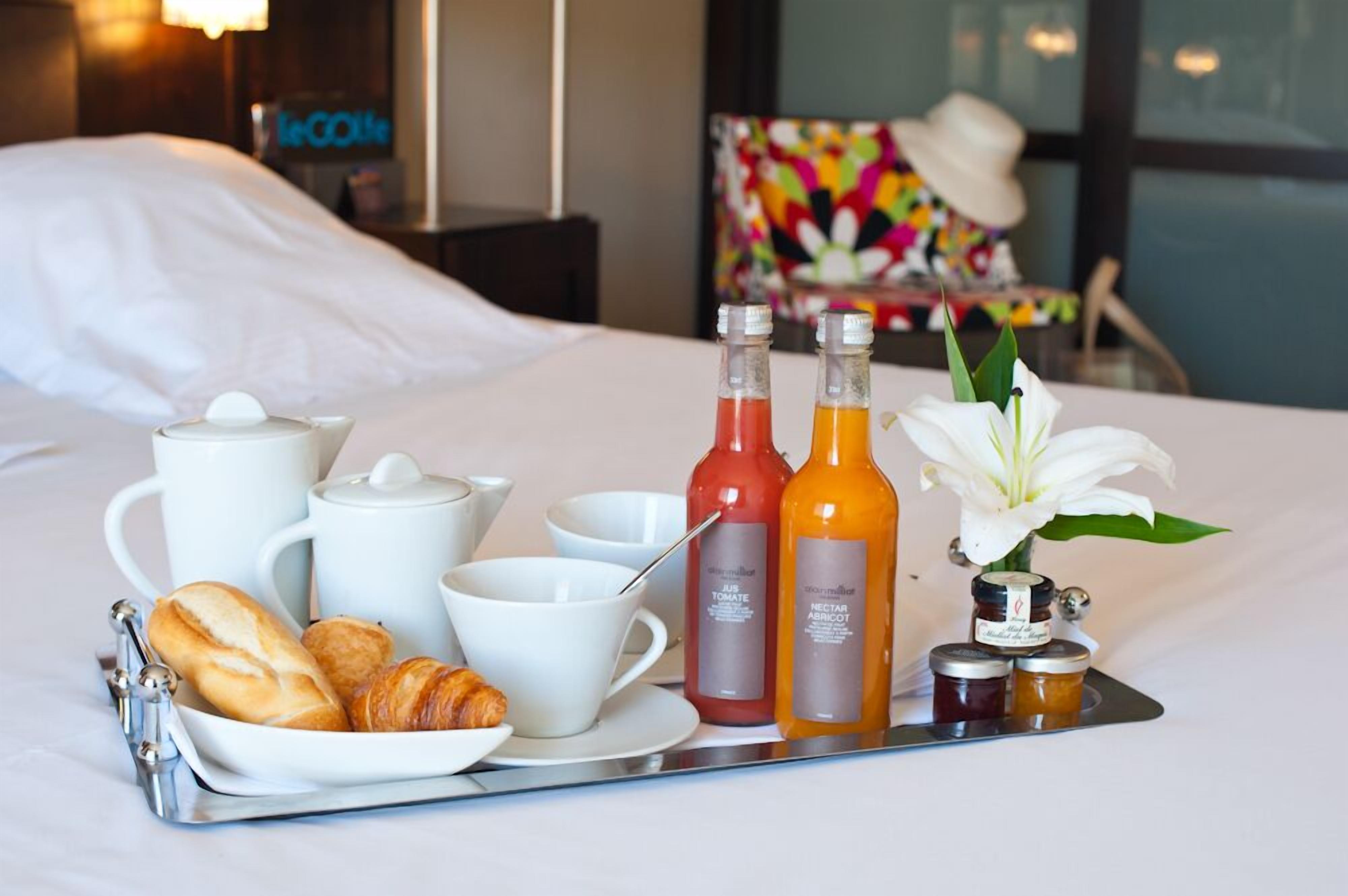 Een ontbijttafel met croissants, koffiekopjes en flesjes sap op een hotelbed.