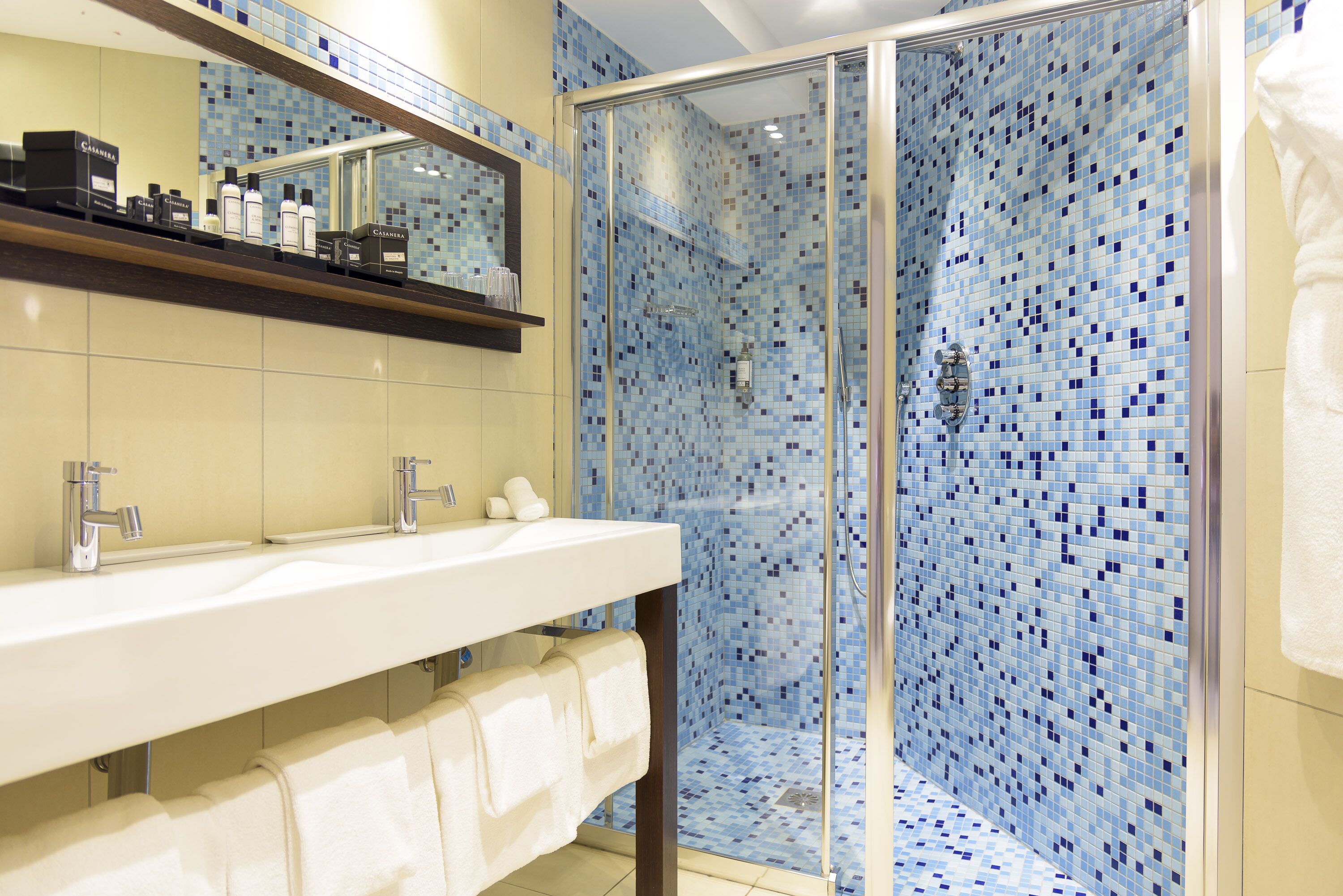 Ein Badezimmer mit einer gläsernen Dusche, einem Doppelwaschtisch und einem Spiegel über dem Waschbecken.