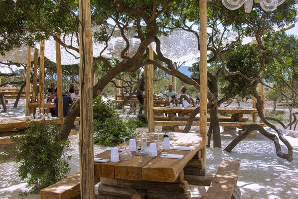 An outdoor dining area with wooden tables and benches, surrounded by trees. - Hôtel Le Golfe (Serra-di-Ferro)