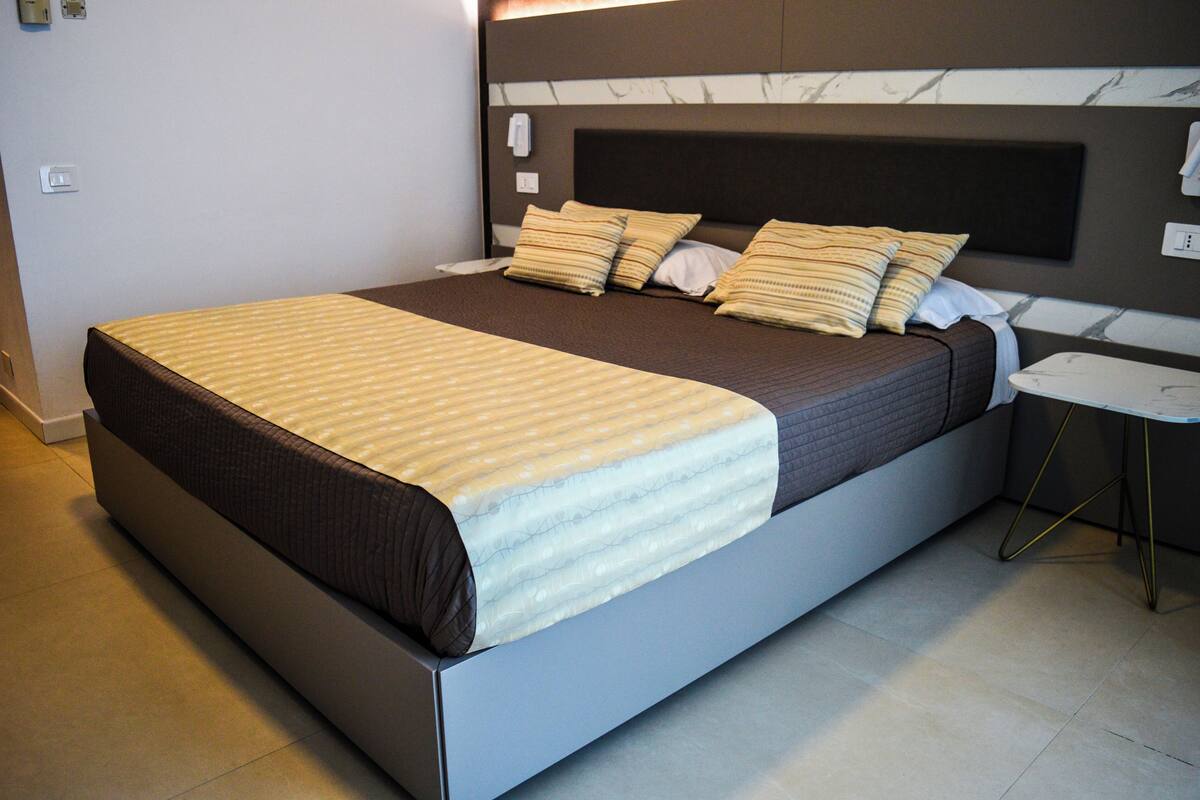 A modern hotel room with a large bed, a bedside table, and a nightstand.