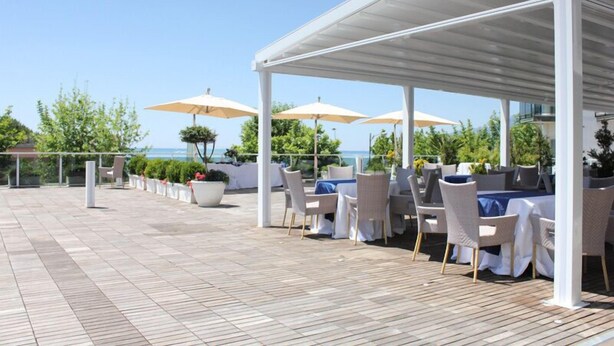 Terrassa exterior amb taules i caires, ombrel·les i vista al mar.