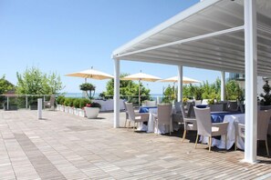 An outdoor patio with tables and chairs, umbrellas, and a view of the sea. - Mediterranea Hotel & Convention Center (Salerno)