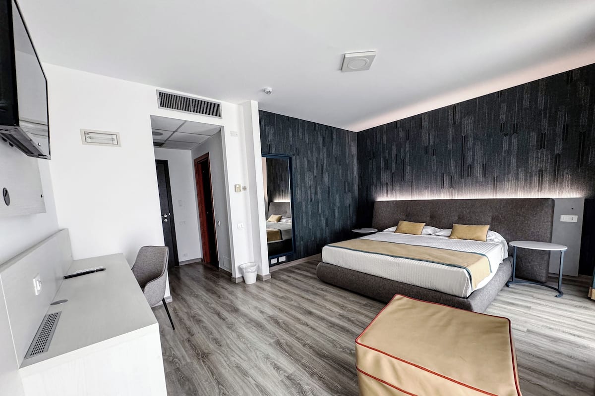 A modern hotel room with a large bed, a desk, a chair, and a small table.