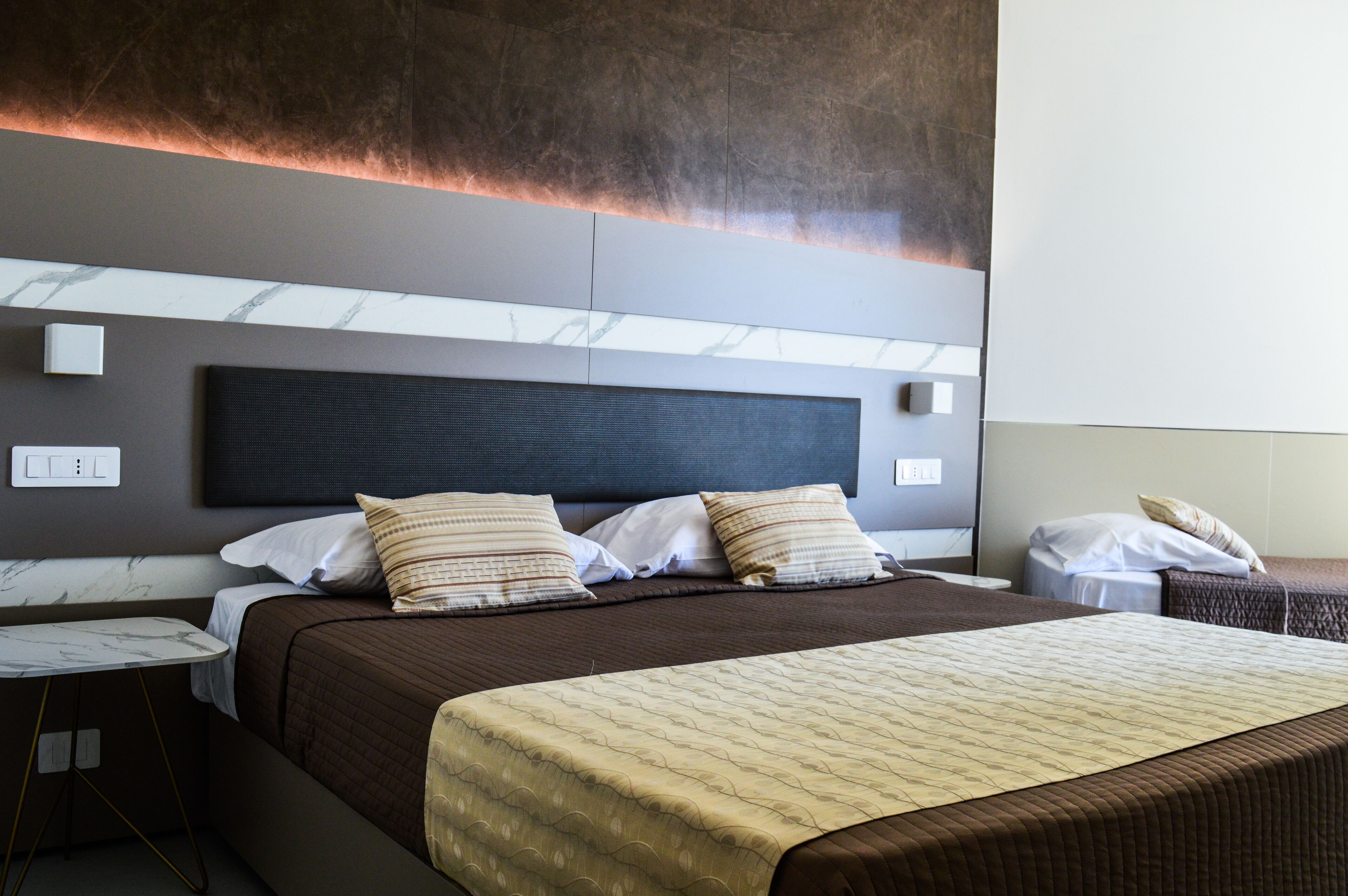 Ein modernes Hotelzimmer mit einem großen Bett, einem мраморнем Nachttisch und einem Kopfteil mit integrierter Beleuchtung.