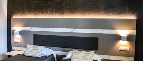 Habitación de hotel con dos camas, cada una con cabecera, mesitas de noche e iluminación empotrada.
