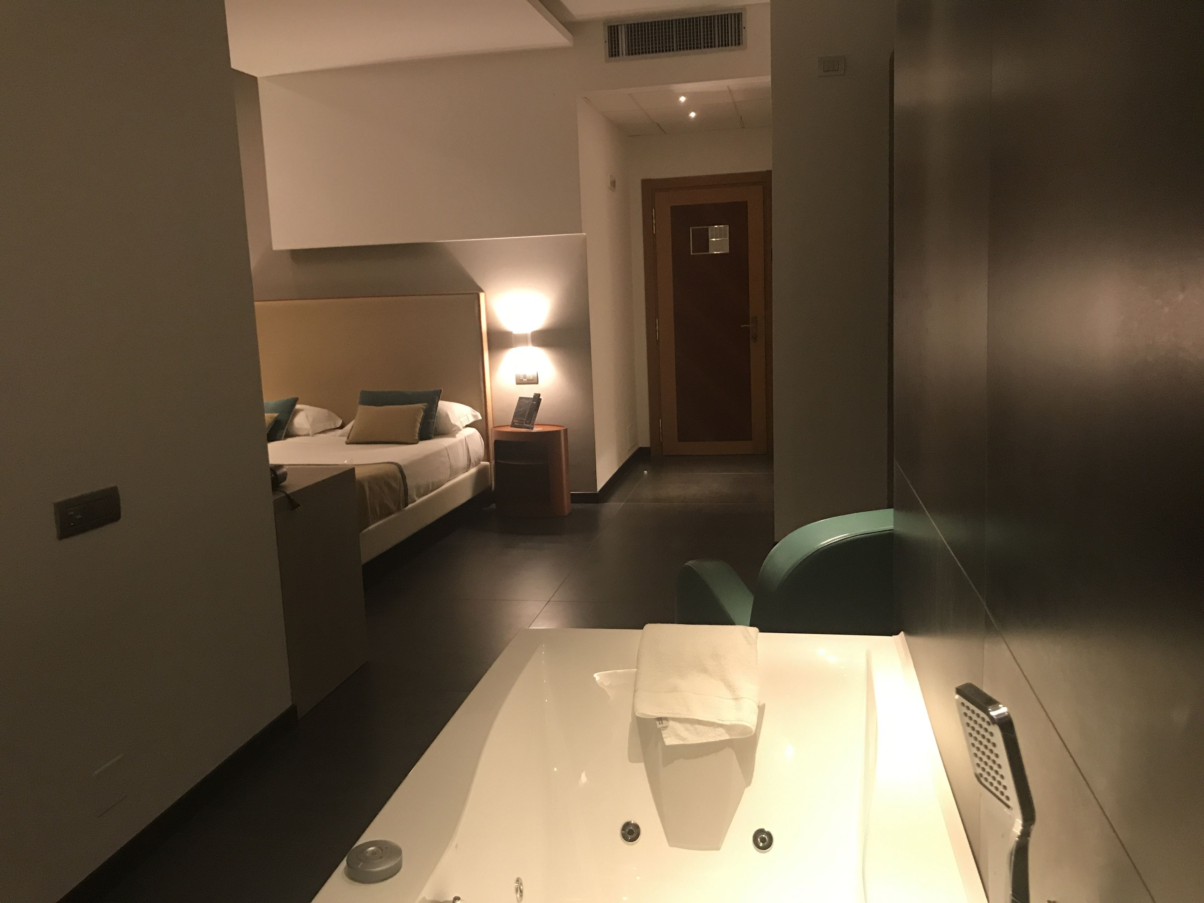 A hotel room with a bed, bedside table, lamp, and a bathtub.