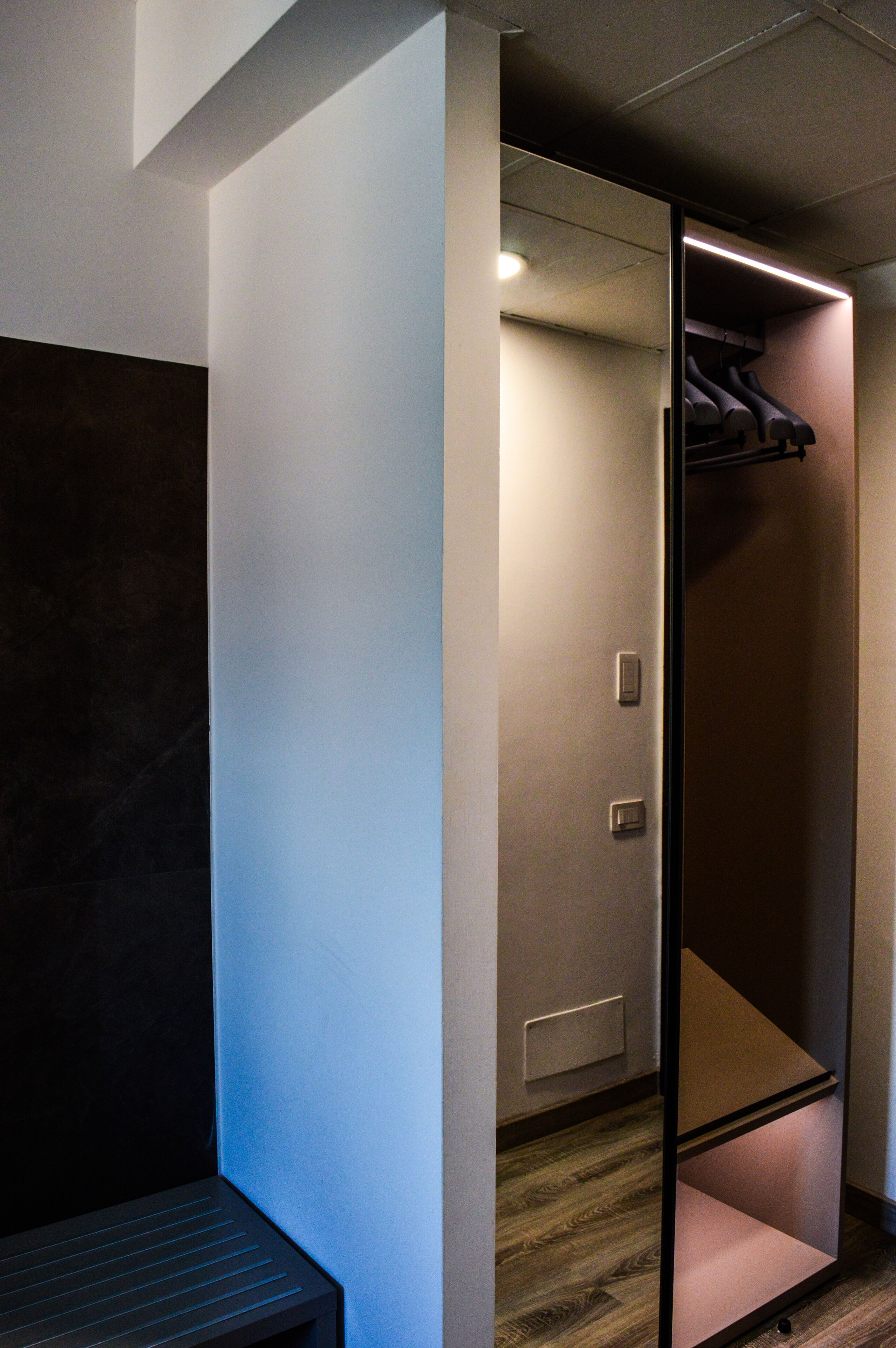A modern hotel room with a sliding door closet, a built-in bench, and a small shelf.