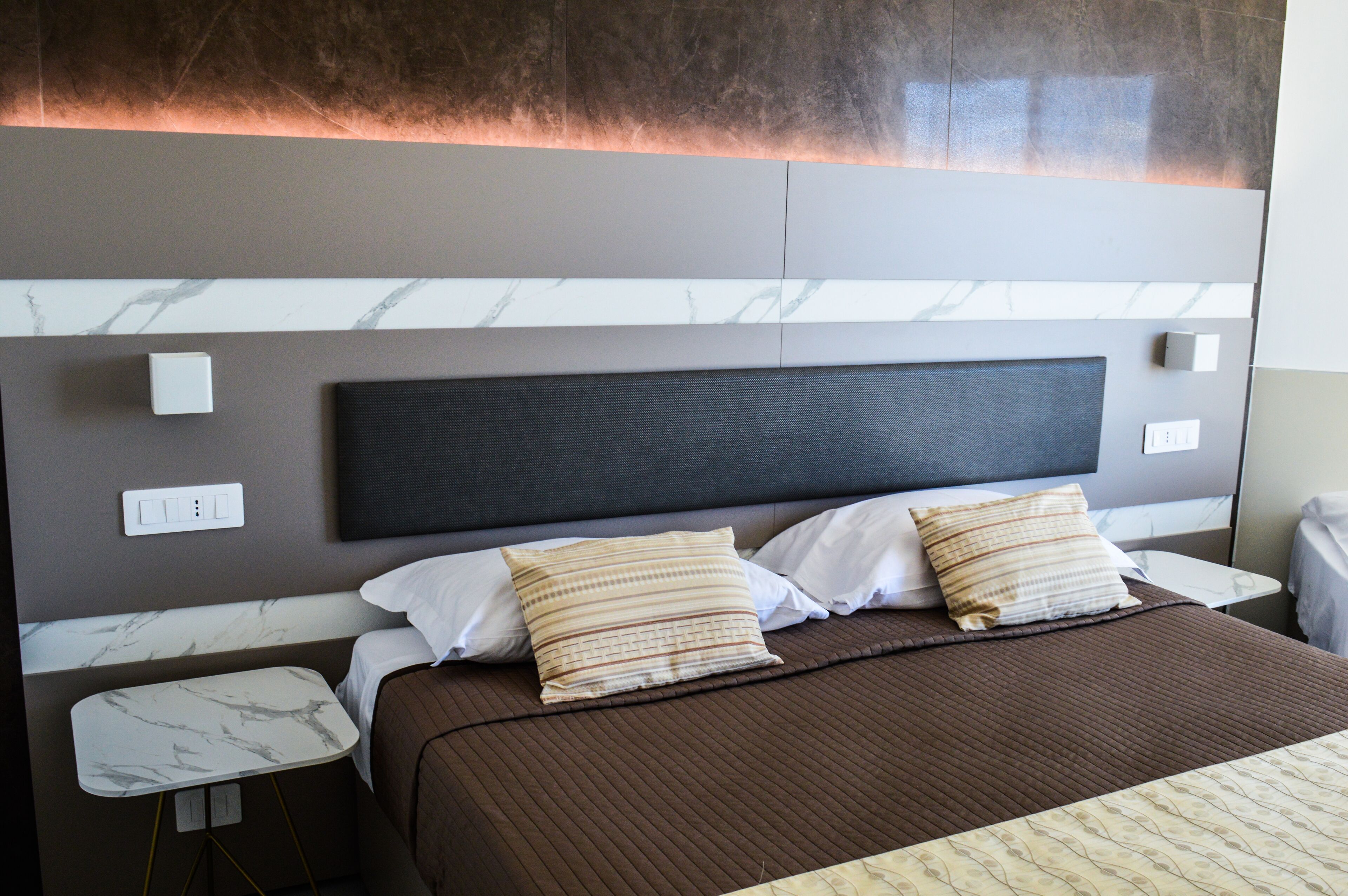 A modern hotel room with a large bed, marble-patterned nightstands, and a wall-mounted light fixture.