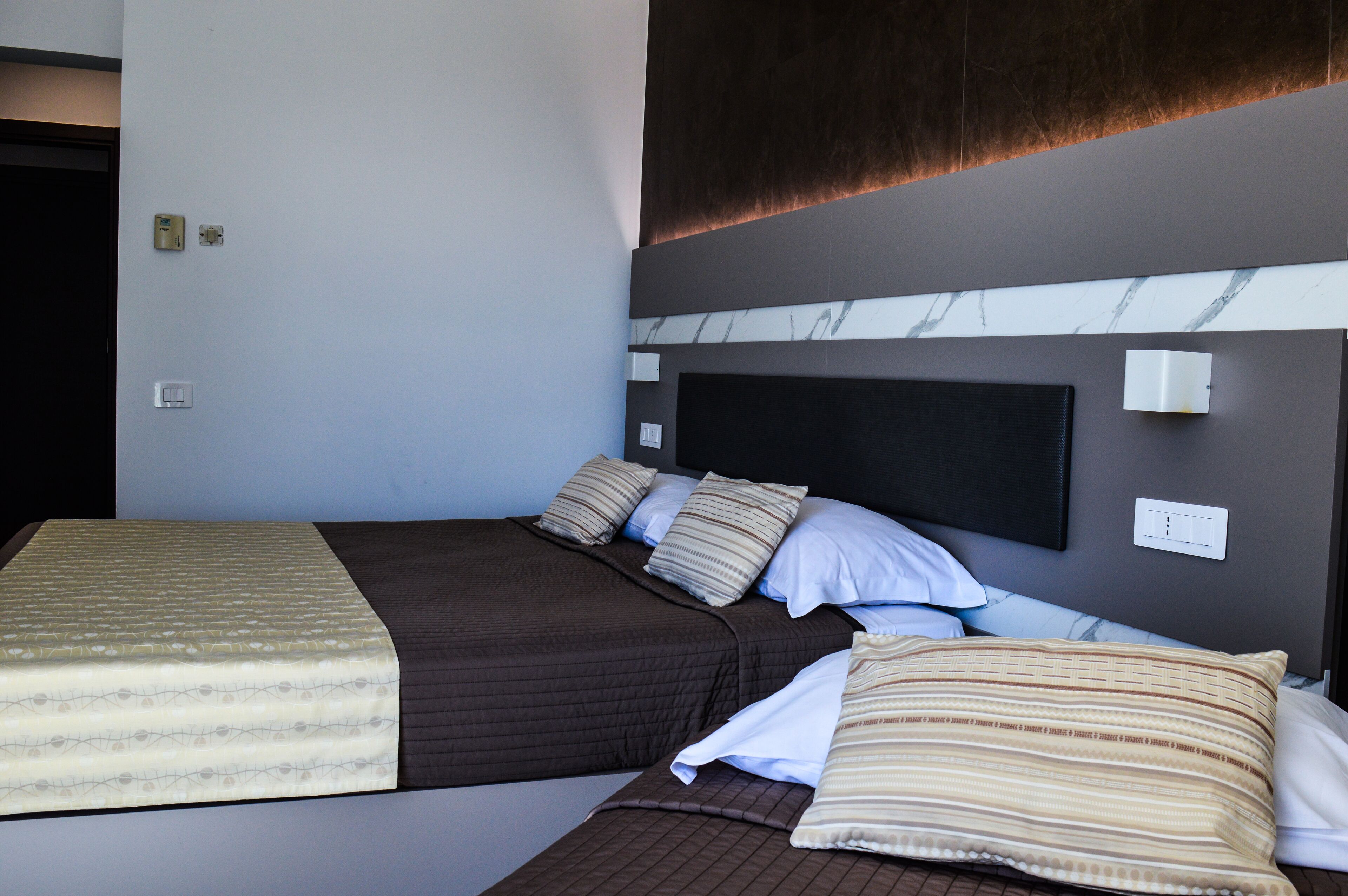 A hotel room with a bed, a headboard, and a wall-mounted light fixture.