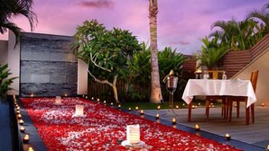 A romantic outdoor dining area with a table set for two, surrounded by a pathway of red flower petals and candles. - Bali Island Villas and Spa Seminyak (Seminyak)