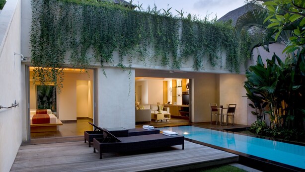 A modern outdoor pool area with a wooden deck, lounge chairs, and a small seating area. - Bali Island Villas and Spa Seminyak (Seminyak)
