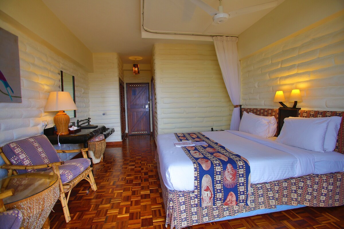 A hotel room with a bed, a chair, a desk, and a door.