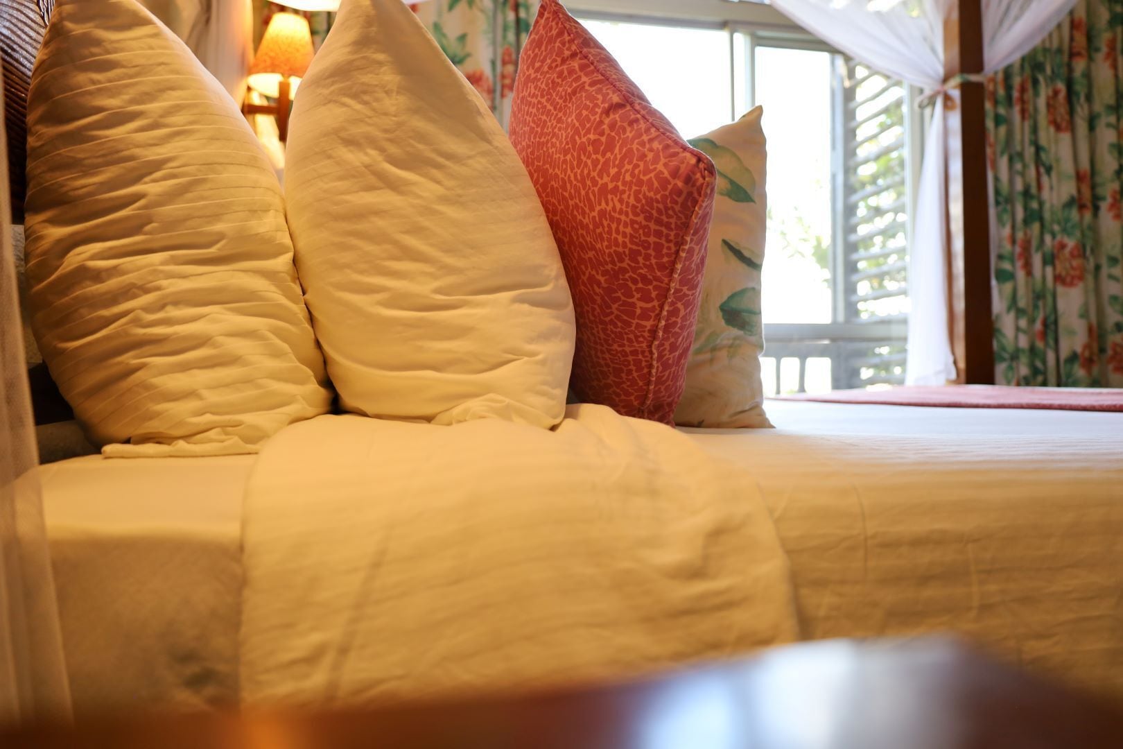 A bed with multiple pillows, a canopy, and a window with floral curtains.