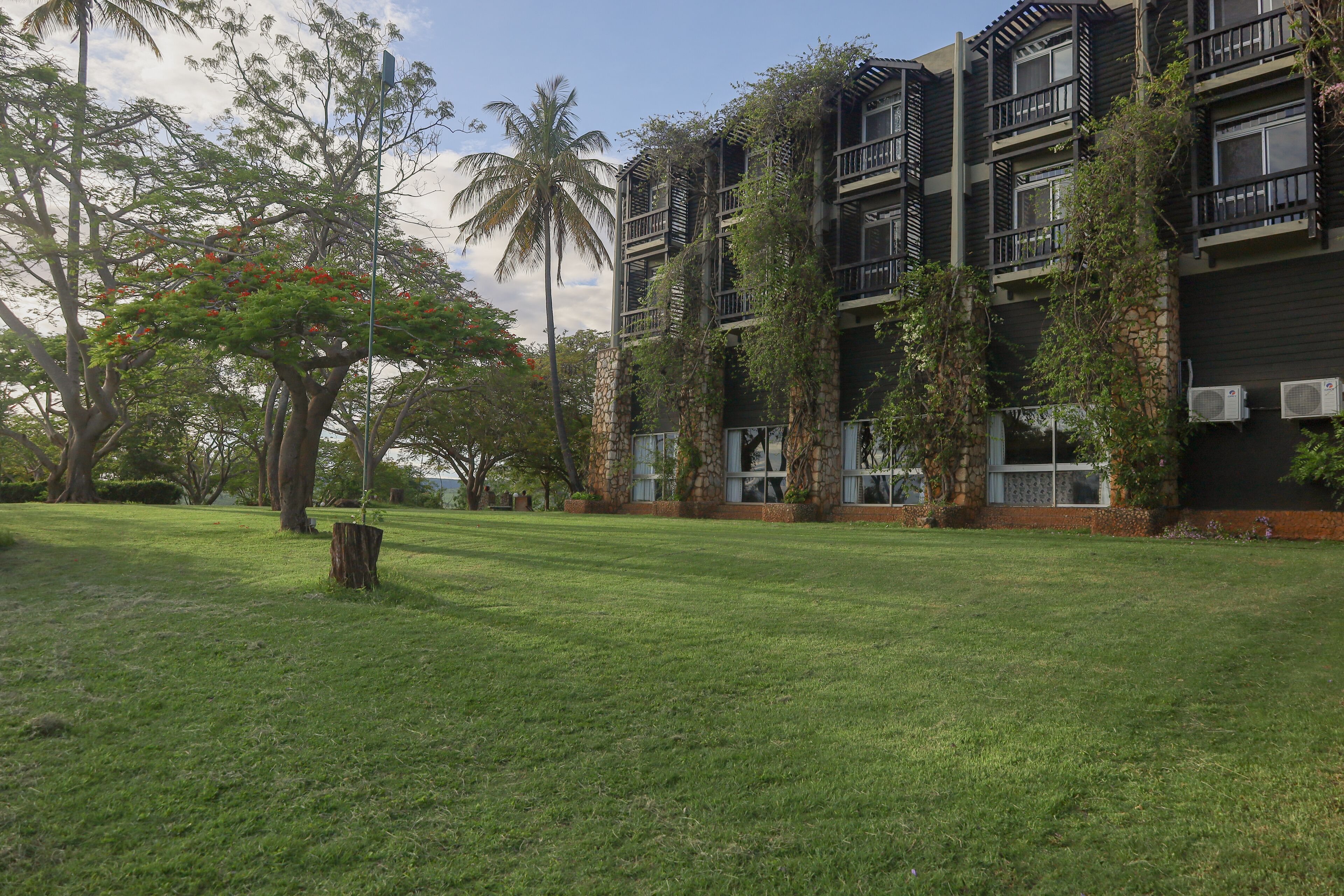 A multi-story building with balconies and air conditioning units, surrounded by a well-maintained lawn and trees.