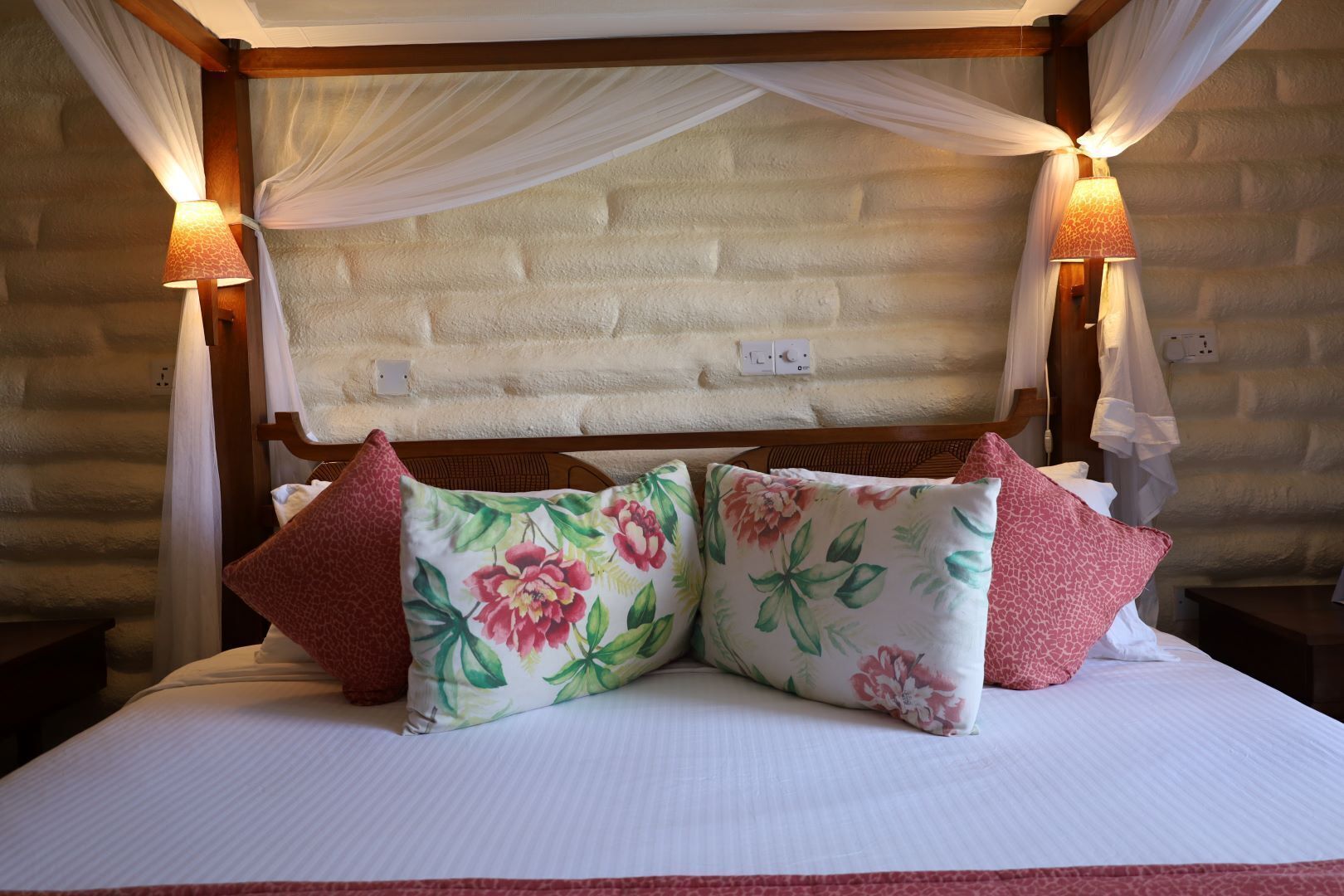 A bed with a canopy, floral pillows, and two bedside lamps.