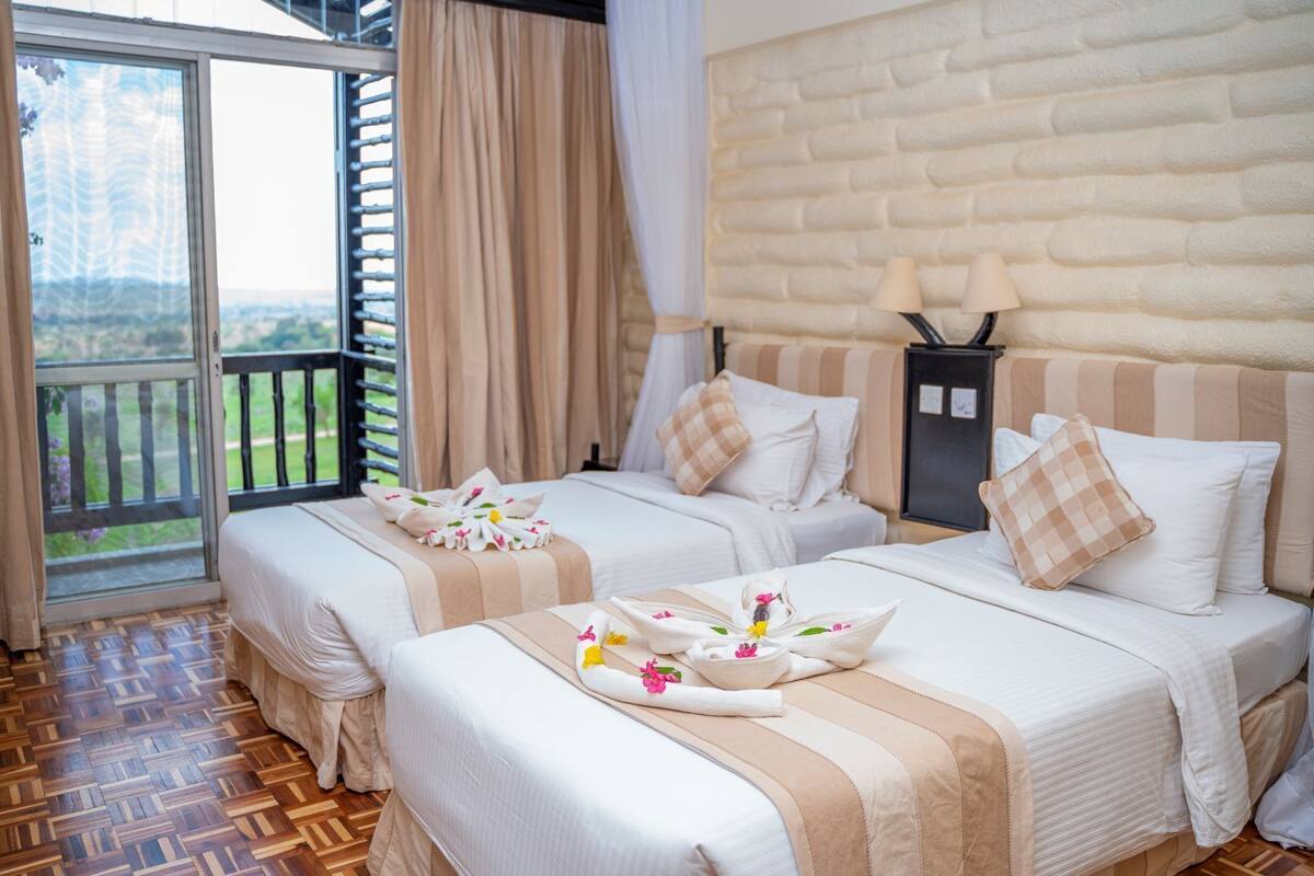 Une chambre d’hôtel avec deux lits, un balcon et un mur à la texture de pierre.