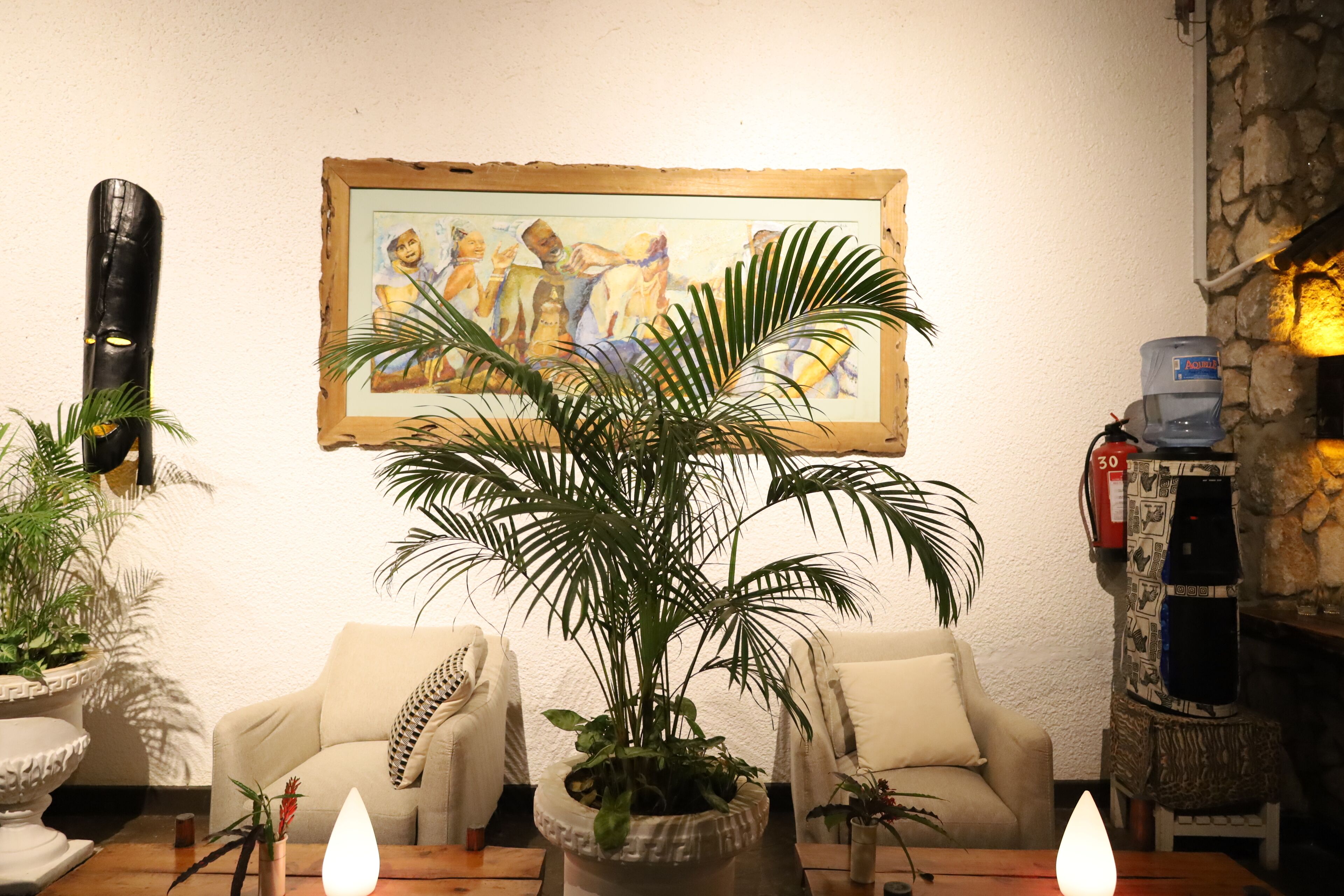 Ein Wohnzimmer mit einer großen Topfpflanze, zwei Sofas, einem Gemälde an der Wand und einem Wasserspender.