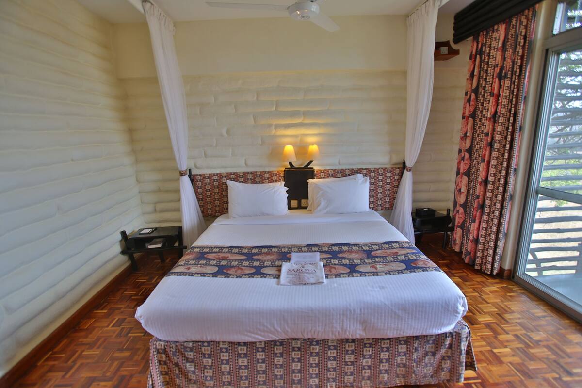 Une chambre à coucher avec un lit, une table de chevet, une lampe fixée au mur et une fenêtre avec des rideaux.