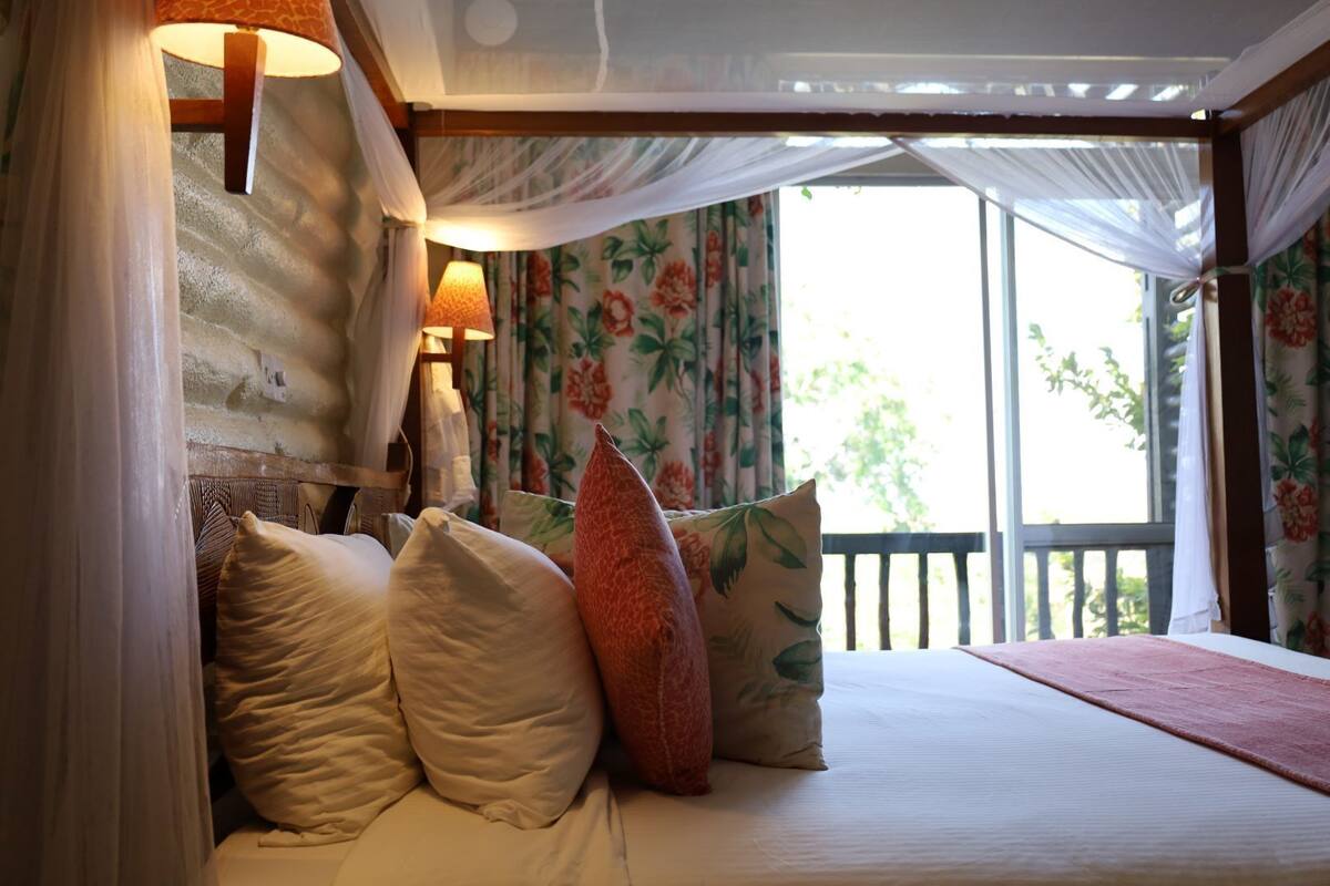 Une chambre à coucher avec un lit, des oreillers, une table de chevet, une lampe et des rideaux.